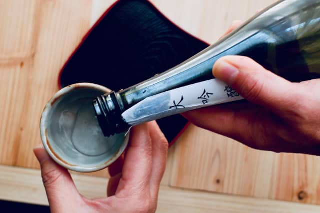 Pouring sake from a bottle labeled daiginjo into an ochoko