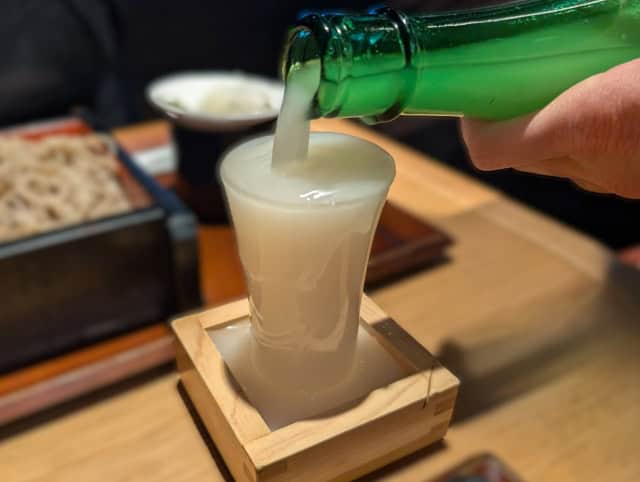 Nigori sake poured overflowing into a traditional wooden masu
