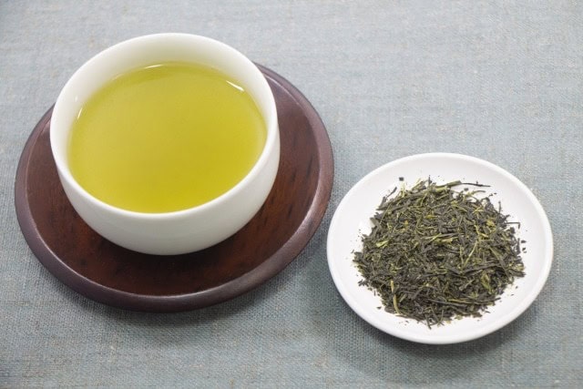 Gyokuro tea brewed in a cup next to a plate of dried gyokuro leaves