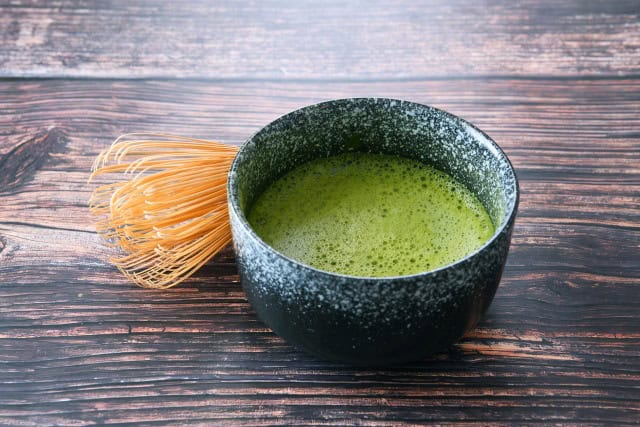 Bowl of freshly whisked matcha with a bamboo whisk on a wooden table