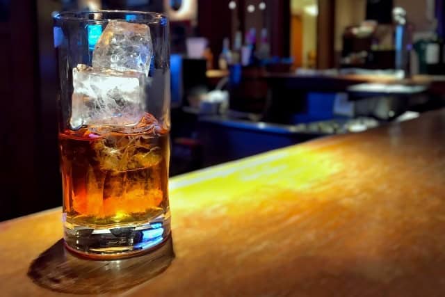 Glass of Japanese whisky with large ice cube on a bar counter