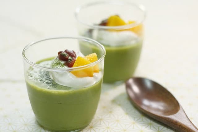 Matcha pudding topped with cream, red beans, and mango in glass cups