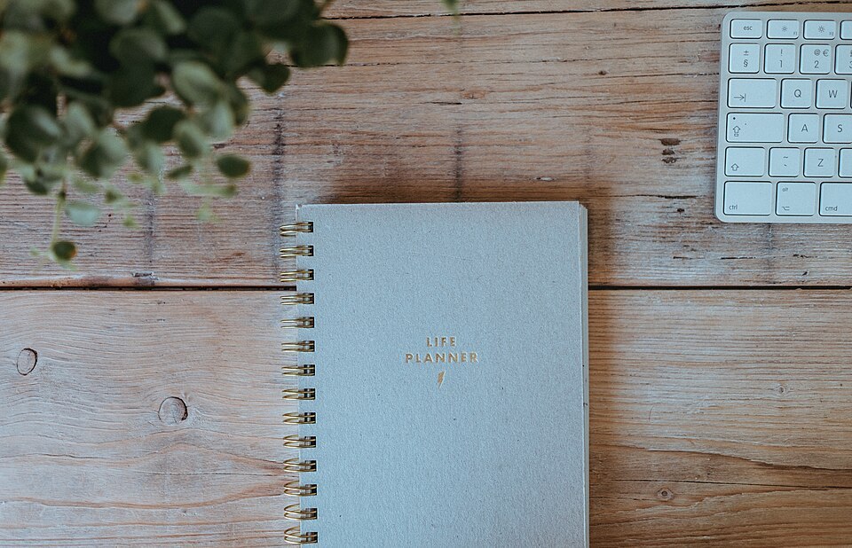 Spiral-bound planner on a wooden desk beside a keyboard