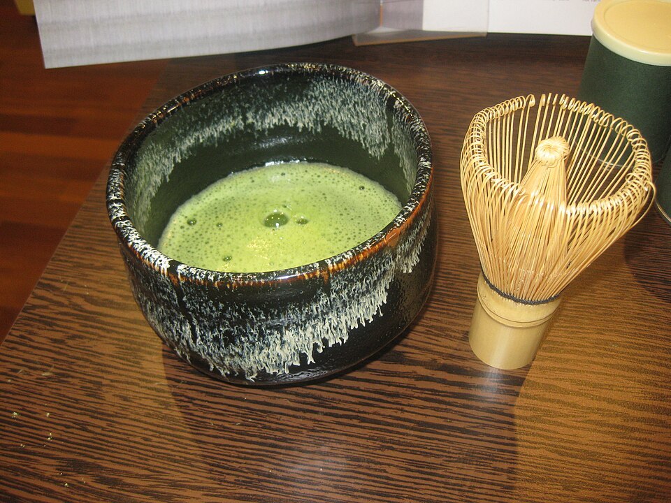 Bowl of whisked green matcha beside a bamboo whisk