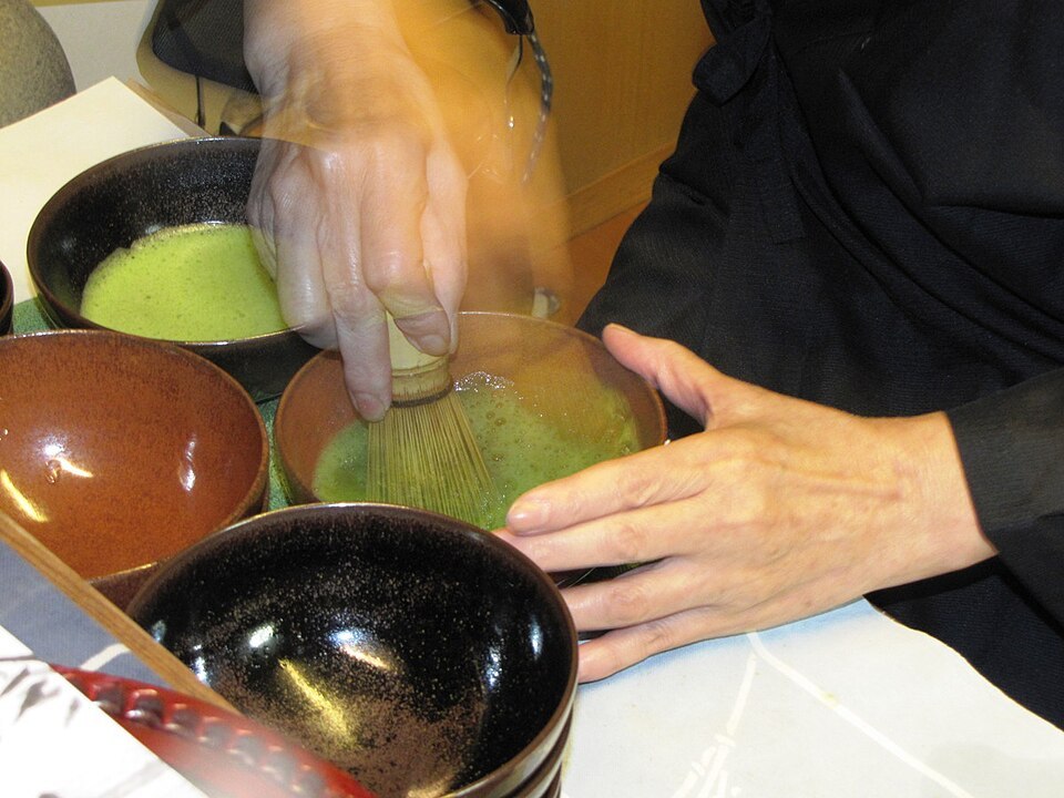Hands whisking matcha in a bowl during tea preparation